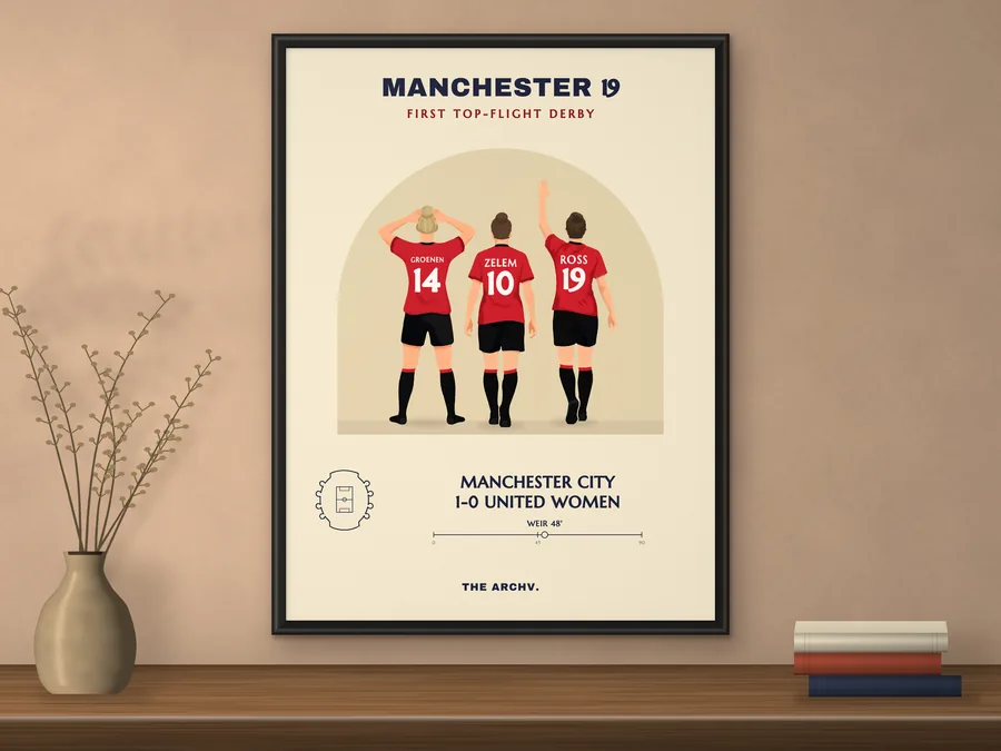 Framed poster on a wall: Manchester United Women v Manchester City, the first WSL Manchester derby, 2019, three players seen from behind in red and black.